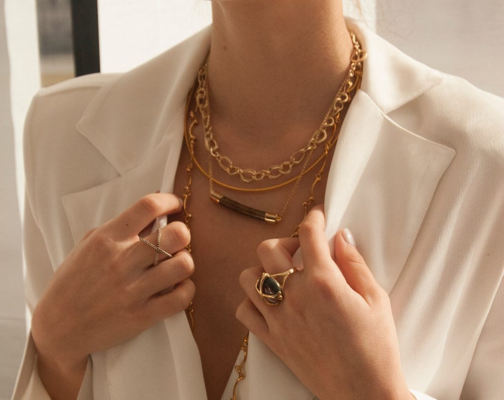 woman wearing timeless white silk top with gold rings and gold layered necklaces